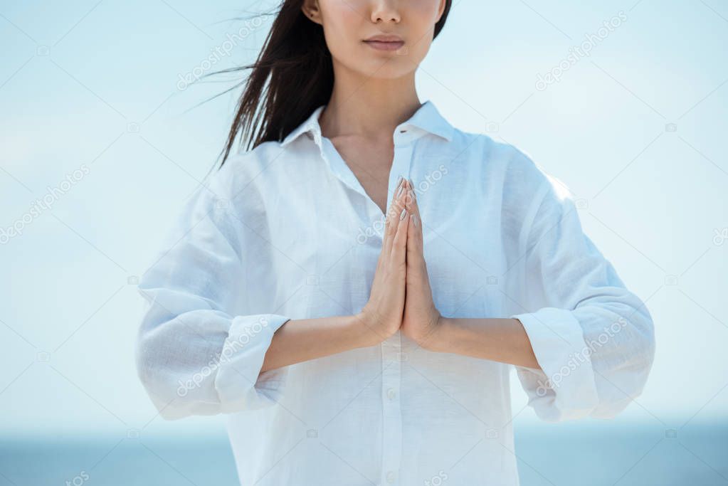 cropped image of asian woman doing namaste mudra gesture on beach 