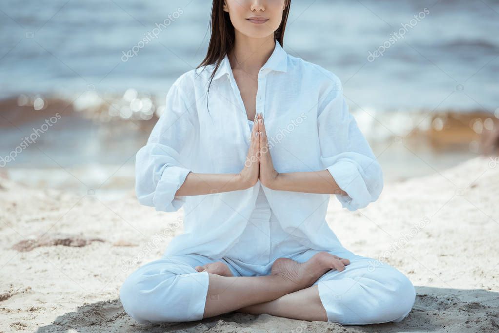 cropped image of woman in anjali mudra (salutation seal) pose on beach by sea 