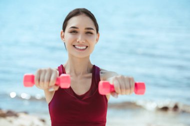 Asya sporcumuz deniz önünde dumbbells ile egzersiz gülümseyen