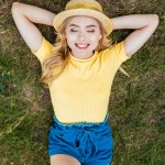 Vista aérea de la joven sonriente en sombrero descansando sobre hierba verde en el parque