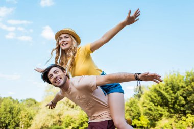 low angle view of happy couple piggybacking in park clipart