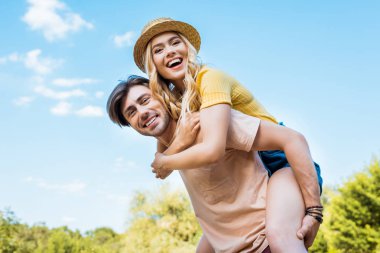 low angle view of happy couple piggybacking in park clipart