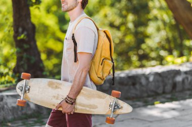 adam sırt çantası ve longboard Caddesi üzerinde gülümseyen kısmi görünümü