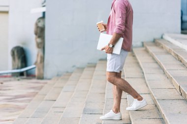 adam sokakta basamaklarda yürüyüş dizüstü bilgisayar ve kahve kısmi görünümü