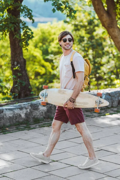 Vista Lateral Sonreír Gafas Sol Hombre Con Mochila Longboard Calle — Foto de Stock