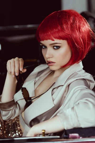 Όμορφη Νεαρή Γυναίκα Κόκκινη Περούκα Κρατώντας Γυαλιά Ηλίου Ενώ Κάθεστε — Δωρεάν Φωτογραφία