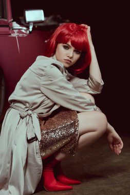 güzel şık genç kadın arabanın yakınında çömelme sırasında kameraya bakıyor 