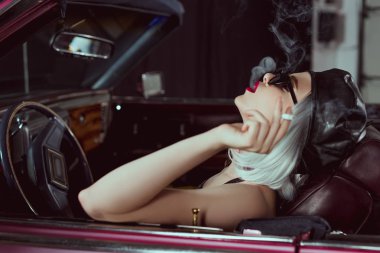 Şehvetli sarışın kadın güneş gözlüğü ve bere retro arabada sigara içilmeyen yan görünüm 