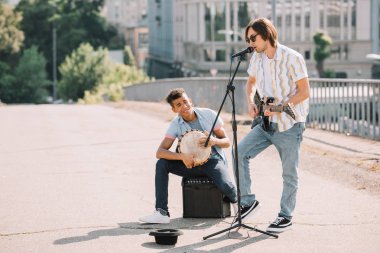 Genç ve mutlu erkek sokak müzisyenleri gitar ve djembe City oynamak