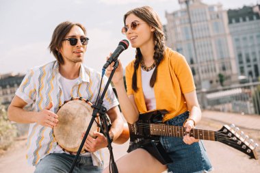 Male and female young people with guitar and djembe performing on street clipart