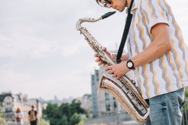Young hipster man with saxophone performing on street clipart