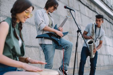 Multiracial young musical band with guitar, drum and saxophone performing on street