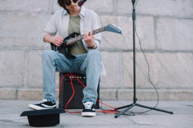 Sokak çalgıcısının önündeki boş şapka şehir ortamında gitar çalıp şarkı söylüyor.