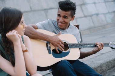 Multiracial young people playing guitar and singing on street clipart