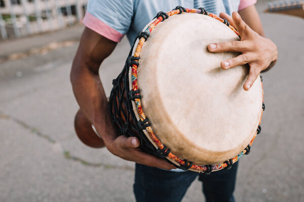 Cropped view of african american street musician playing djembe in city