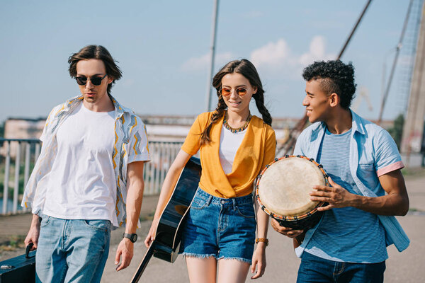 Young and happy street musicians carrying instruments in city