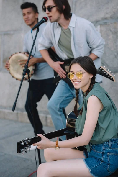 Multiracial young people with guitars and djembe performing on street