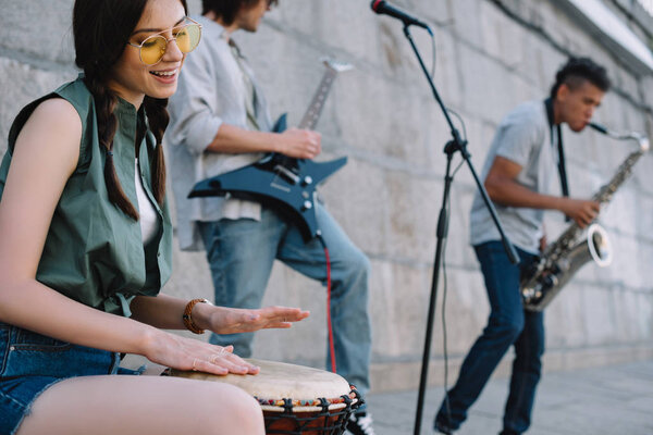 Happy woman and men with musical instruments performing on sunny city street