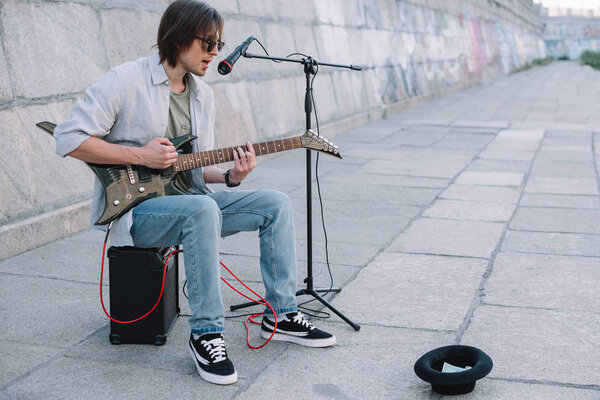 Young happy busker playing guitar and singing at city street