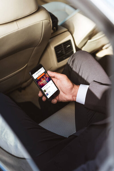 cropped image of businessman holding smartphone with loaded soundcloud page in car