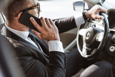 araba ve smartphone ile konuşmaya takım elbise içinde yakışıklı sürücü yan görünüm