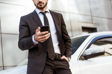akıllı telefon tutarak ve arabanın yakınında duran işadamı kırpılmış görüntü