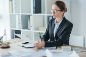 attractive financier working with documents at table in office 
