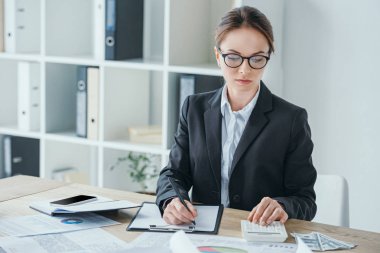 attractive financier working at table in office with calculator and clipboard clipart