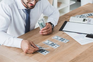 cropped image of business adviser counting dollar banknotes on table in office clipart