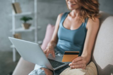 cropped image of woman shopping online with laptop and credit card at home