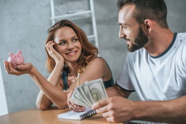 happy couple planning family budget and looking at each other in living room clipart