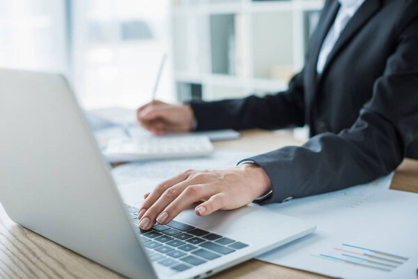cropped image of financier using laptop at table in office