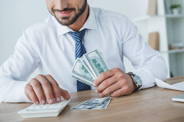 cropped image of business adviser counting money with calculator in office