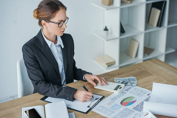 high angle view of financier working at table in office with calculator and clipboard