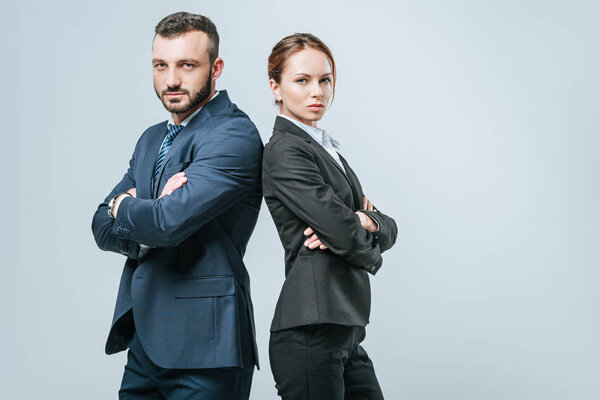 businesswoman and businessman standing with crossed arms and looking at camera isolated on grey