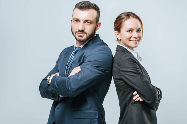 smiling businesswoman and businessman standing with crossed arms and looking at camera isolated on grey