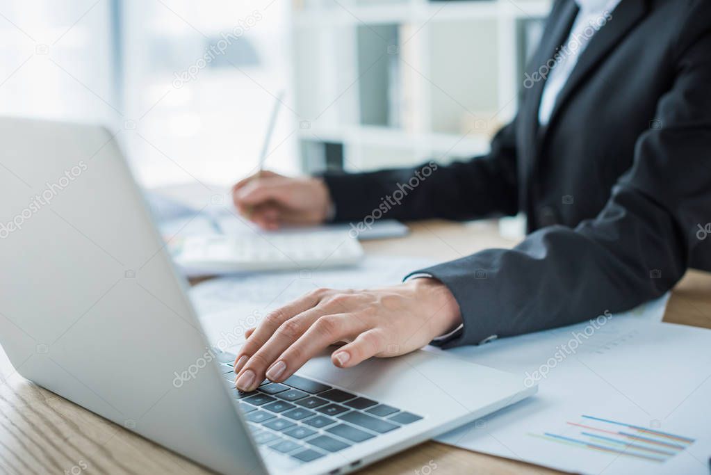 cropped image of financier using laptop at table in office