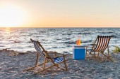 nyári italok a hűvösebb és a hintó társalgók, homokos tengerparton naplementekor 