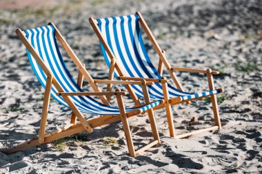 striped beach chairs and cooler on sandy coast clipart