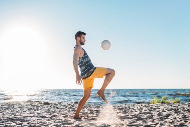 handsome young man playing with ball on sandy beach clipart