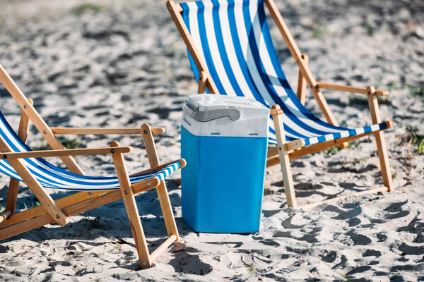 striped beach chairs and cooler on sand 