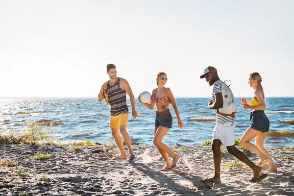 Felices Jóvenes Amigos Multiétnicos Con Pelota Mochilas Caminando Juntos Playa —  Fotos de Stock