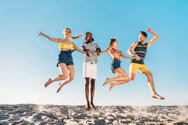 Happy Young Multiethnic Friends Holding Hands Jumping Sandy Beach — Stock Photo, Image