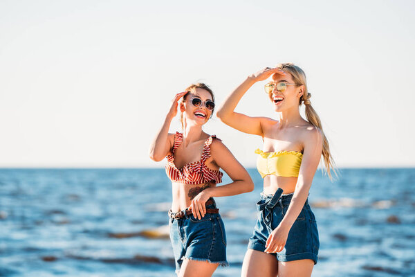 happy young women in sunglasses walking together on beach
