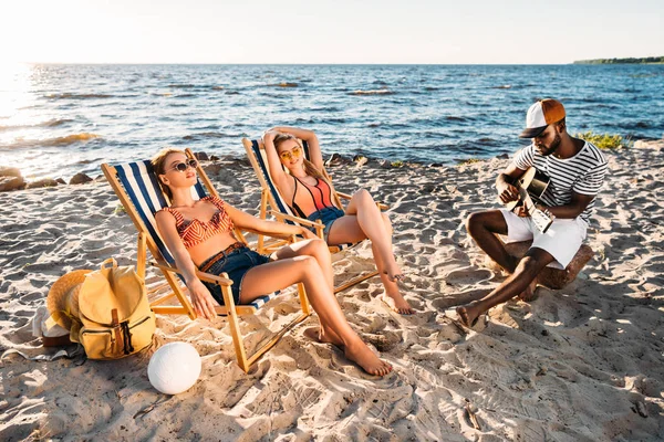 Hermosas Mujeres Jóvenes Descansando Sillas Playa Hombre Afroamericano Tocando Guitarra — Foto de Stock