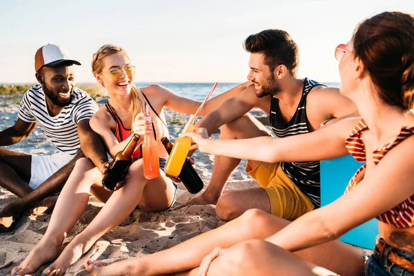 Happy Young Multiethnic Friends Clinking Glass Bottles Drinks While Sitting — Stock Photo, Image