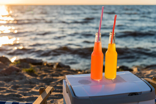 close-up view of summer drinks with straws and cooler on sandy beach at sunset