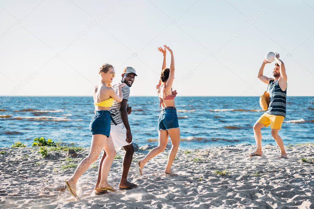young multiethnic friends playing volleyball on sandy beach 