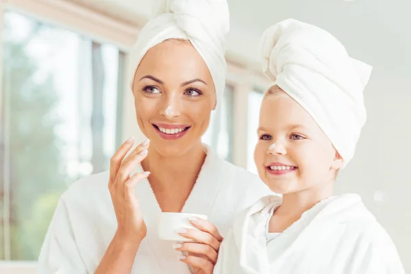 Atractiva Sonriente Madre Hija Batas Baño Toallas Aplicando Crema Facial —  Fotos de Stock