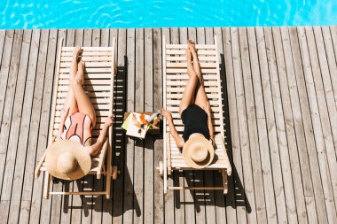 high angle view of young women resting on chaise lounges near swimming pool    clipart